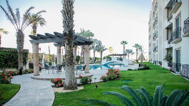 A hotel courtyard with a pool, palm trees, and outdoor seating. - Condo PC by TRVL2HM (Cabo San Lucas)