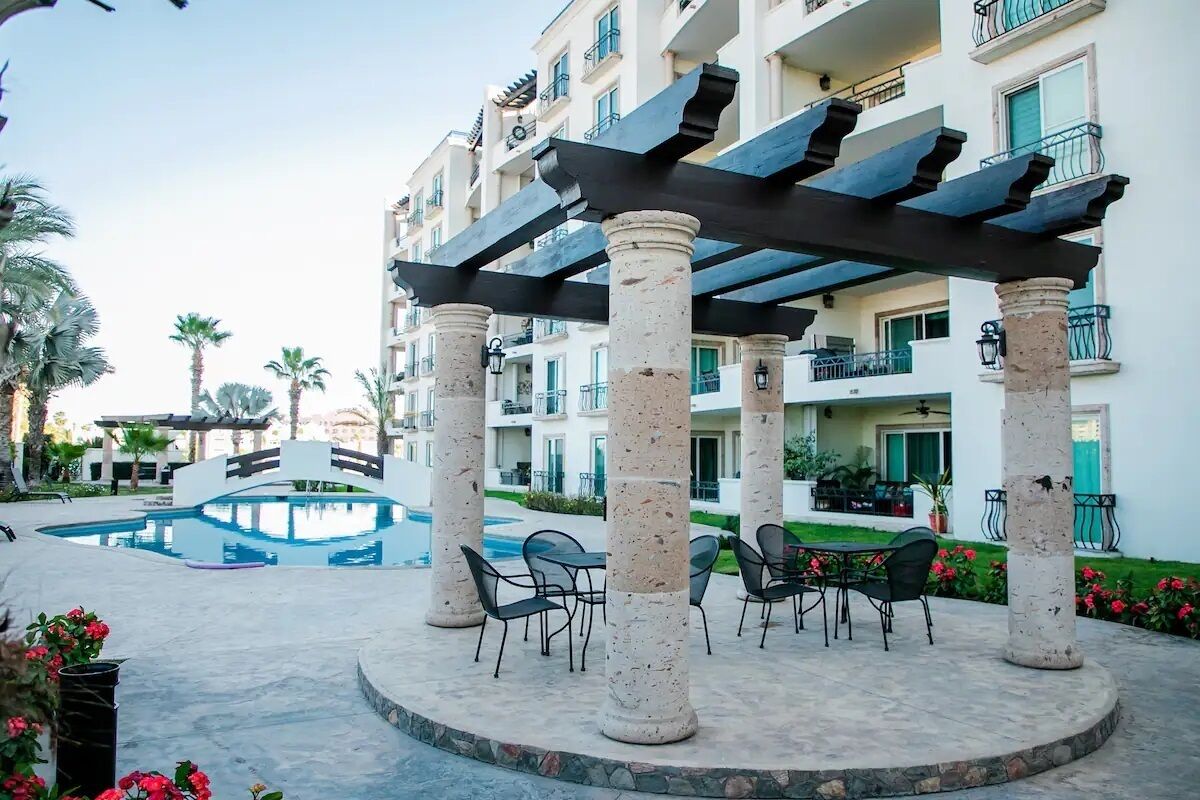 A hotel courtyard with a pool, outdoor seating, and a covered area with columns.