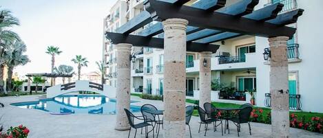 A hotel courtyard with a pool, outdoor seating, and a covered area with columns.