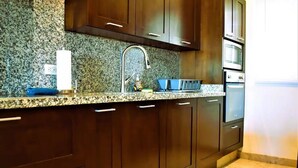 A kitchen with dark wooden cabinets, a granite countertop, a stainless steel sink, and a built-in oven. - Condo PC by TRVL2HM (Cabo San Lucas)