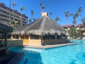 A pool area with a thatched-roof structure, palm trees, and a clear blue sky. - CONDO MRS BY TRVL2HM (Cabo San Lucas)