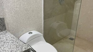 A bathroom with a toilet, a shower with a glass door, and a patterned wall. - CONDO MRS BY TRVL2HM (Cabo San Lucas)