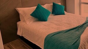 A neatly made bed with white linens and teal pillows, a teal throw blanket, and a wooden floor. - CONDO MRS BY TRVL2HM (Cabo San Lucas)