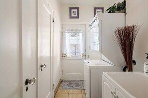 A narrow hallway with a door, a window with curtains, a washing machine, and a small rug. - Trick or Treat, Relax and Retreat (Stockton)
