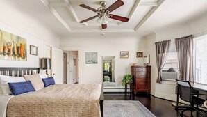 Quarto com cama, escrivaninha, cadeira, ventilador de teto e vista para o exterior.