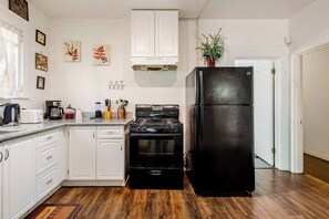 Una cocina con gabinetes blancos, un refrigerador negro, una estufa y una cafetera.