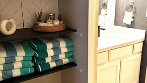 A bathroom with a white sink, a mirror, and a towel rack. There are shelves with folded towels and a basket with toiletries. - Casa Arizu, w/ rv parking and private pool (Lake Havasu City)
