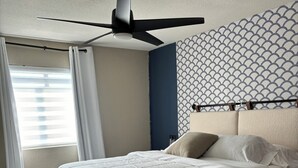 A bedroom with a bed, a ceiling fan, a window with curtains, and a patterned wall. - Casa Arizu, w/ rv parking and private pool (Lake Havasu City)