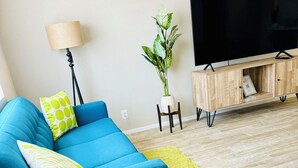 A modern living room with a blue sofa, a green rug, a potted plant, a wooden cabinet, and a television. - Casa Arizu, w/ rv parking and private pool (Lake Havasu City)