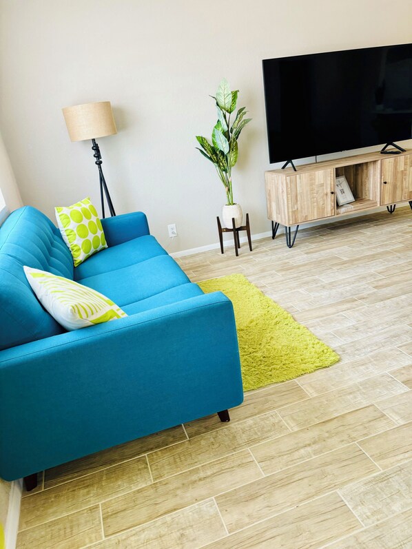 A modern living room with a blue sofa, a green rug, a potted plant, a wooden cabinet, and a television. - Casa Arizu, w/ rv parking and private pool (Lake Havasu City)