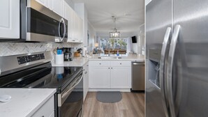 Cozinha moderna com armários brancos, eletrodomésticos de aço inoxidável e backsplash de azulejos em padrão herringbone.