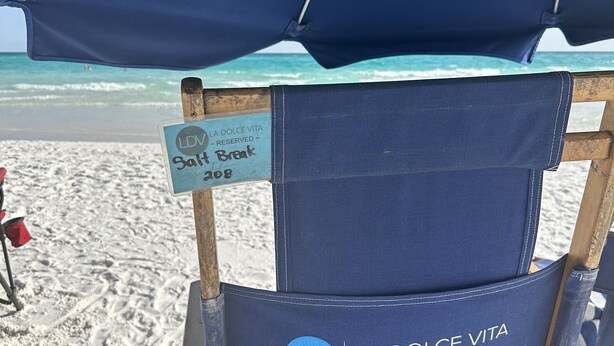Een strandparasol met een bord waarop staat 'Salt Break 208' en 'La Dolce Vita Gereserveerd'.