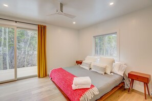 Relax in this serene bedroom with a large bed, two nightstands, and a ceiling fan. Enjoy a view of the surrounding trees from the large window.