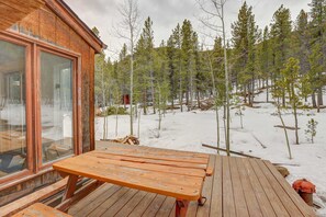 Enjoy outdoor dining or relaxation on the cabin's deck with a picnic table and benches, surrounded by a serene forest view.