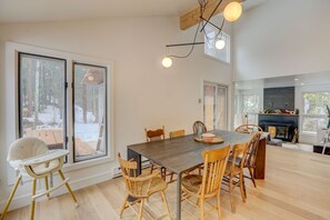 Enjoy meals in this dining area with a large table and comfortable chairs, surrounded by high ceilings and large windows offering views of the outdoors.