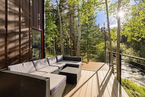 A deck with outdoor furniture, a glass door, and a view of a river. - Updated Cozy Cabin on the River / Hot Tub / Beach (Idaho Springs)