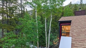 A cabin with a wooden exterior, a red door, and a view of a forested area with trees and a stream.