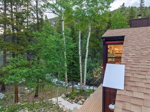 A cabin with a wooden exterior, a red door, and a view of a forested area with trees and a stream. - Updated Cozy Cabin on the River / Hot Tub / Beach (Idaho Springs)