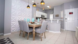 A dining area with a wooden table and grey upholstered chairs, a geometric patterned wall, and pendant lighting.