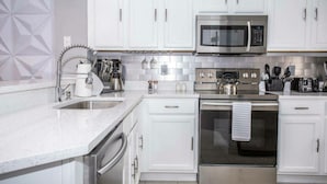 A modern kitchen with white cabinets, stainless steel appliances, and a tiled backsplash.