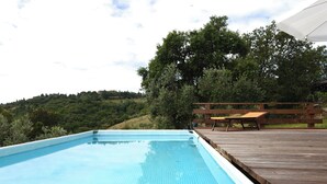 Ein rechteckiger Pool mit Holzterrasse und Liegestühlen.