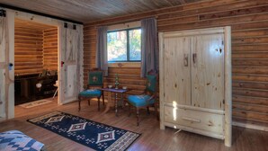 Interior acollidor d'una cabana de fusta amb zona de menjador, dues cadires, una taula i un gran armari de fusta.