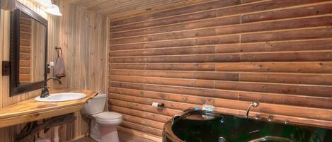 Een badkamer met houten wanden, een houten wastafelmeubel met een wastafel, een toilet en een groot, groen bad.