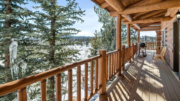 Una terraza de madera con vistas a árboles nevados y un paisaje lejano.