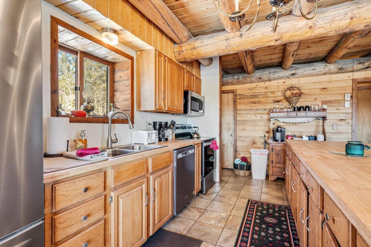 A rustic kitchen with wooden cabinets, a stainless steel refrigerator, a microwave, and a sink.