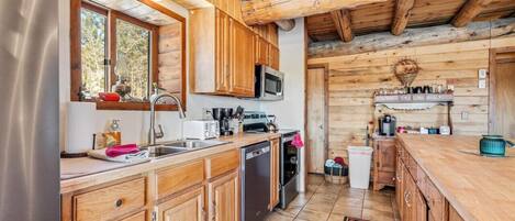 A rustic kitchen with wooden cabinets, a stainless steel refrigerator, a microwave, and a sink.