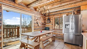 Una cabaña de madera con una zona de cocina que incluye un refrigerador grande, una mesa de comedor con bancos y un candelabro.