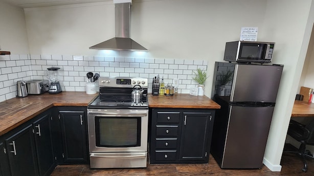A compact kitchen with a stainless steel stove, a microwave, and a refrigerator. There are cabinets, a sink, and a countertop with various kitchen items.