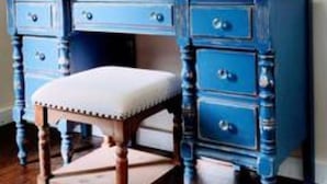 A blue vanity with a mirror, drawers, and a stool.