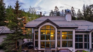 Una casa moderna con un amplio ventanal central, una terraza y una chimenea.