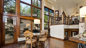 Un comedor amplio con una mesa y sillas de madera, ventanas grandes y una escalera que sube a un nivel superior.