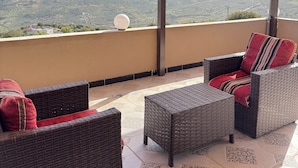 A covered outdoor seating area with wicker furniture and a view of the countryside. - Abu Hossam’s chalet (Souf)