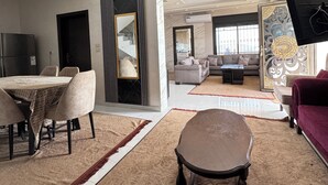 A spacious living area with a dining table, sofas, and a TV mounted on the wall. - Abu Hossam’s chalet (Souf)