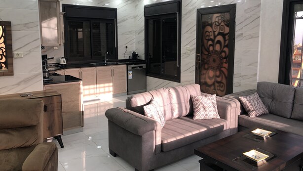 A modern living room with a sofa, coffee table, and a kitchen area with cabinets and a sink. - Abu Hossam’s chalet (Souf)