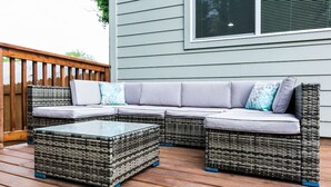 A sectional sofa with cushions, a glass-top coffee table, and wicker furniture on a wooden deck. - EastSide Austin · Quaint 4 Bedroom Eastside Lodge (Pet Friendly & Work Space) (Austin)