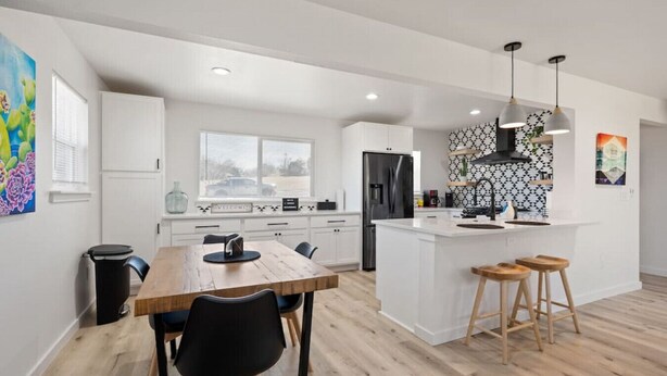 A modern kitchen with white cabinetry, a central island with stools, a black refrigerator, and pendant lighting. - EastSide Austin · Quaint 4 Bedroom Eastside Lodge (Pet Friendly & Work Space) (Austin)