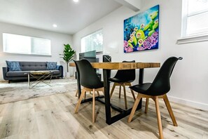 Ein modernes Wohnzimmer mit Esstisch, schwarzen Stühlen, einem grauen Sofa und einem großen Gemälde an der Wand.
