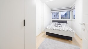 A bedroom with a bed, a window with blinds, and a door.