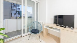 A modern living room with a large TV, a blue chair, and a sliding glass door leading to a balcony.