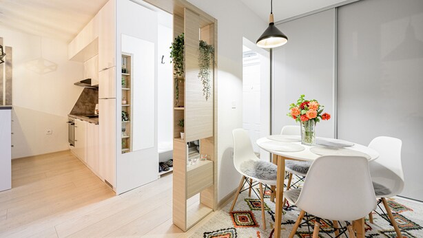 A modern kitchen with white cabinets, a built-in stove, and a wooden countertop. There is a dining area with a white table, chairs, and a vase of flowers.