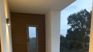 A balcony with wicker chairs and a small table, a window, and a view of a road and trees. - Cosy, upscale apartment in California (Casablanca)
