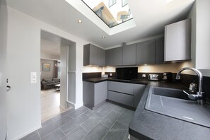 A modern kitchen with grey cabinets, a black countertop, and a skylight.