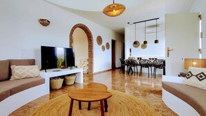 Un salon moderne comprenant un téléviseur, des canapés, une table basse et un coin repas avec des chaises et une table.
