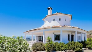 Une villa blanche avec un toit en tuiles, une cheminée centrale et un porche couvert doté de fenêtres.