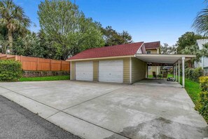 Eine eingeschossige Garage mit zwei weißen Türen, einem roten Dach und einer überdachten Auffahrt.