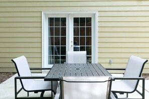 A patio with a table and two chairs, a sliding glass door, and a beige exterior wall.